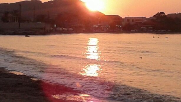A sunset over a calm body of water with buildings in the background. - Christakis Hotel (Corfu)