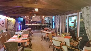 An indoor dining area with tables and chairs, a bar with stools, and a television screen. - Christakis Hotel (Corfu)