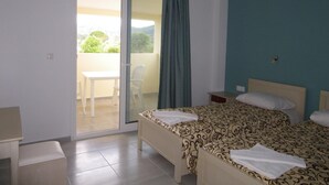 A hotel room with two beds, a balcony with a table and chairs, and a view of greenery outside. - Christakis Hotel (Corfu)