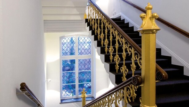 Una escalera con barandales dorados ornamentados y un suelo cubierto de alfombra negra.