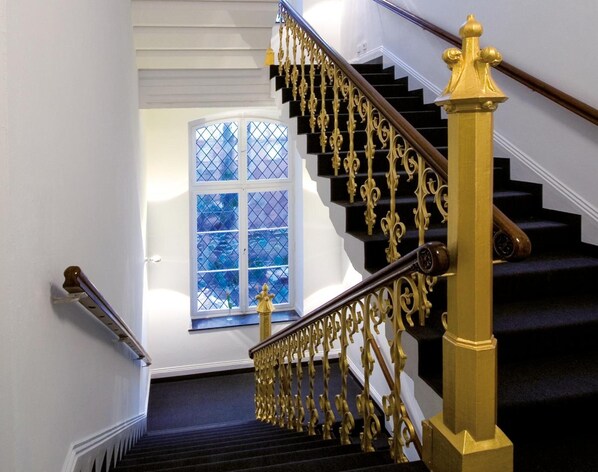 A staircase with ornate golden railings and a black carpeted floor. - Hopper Hotel St. Josef, WorldHotels Crafted (Cologne)