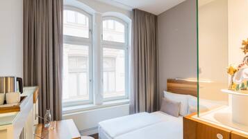 Ein Hotelzimmer mit Bett, Schreibtisch, Stuhl, einer Kaffeemaschine und einem Fenster mit Vorhängen.