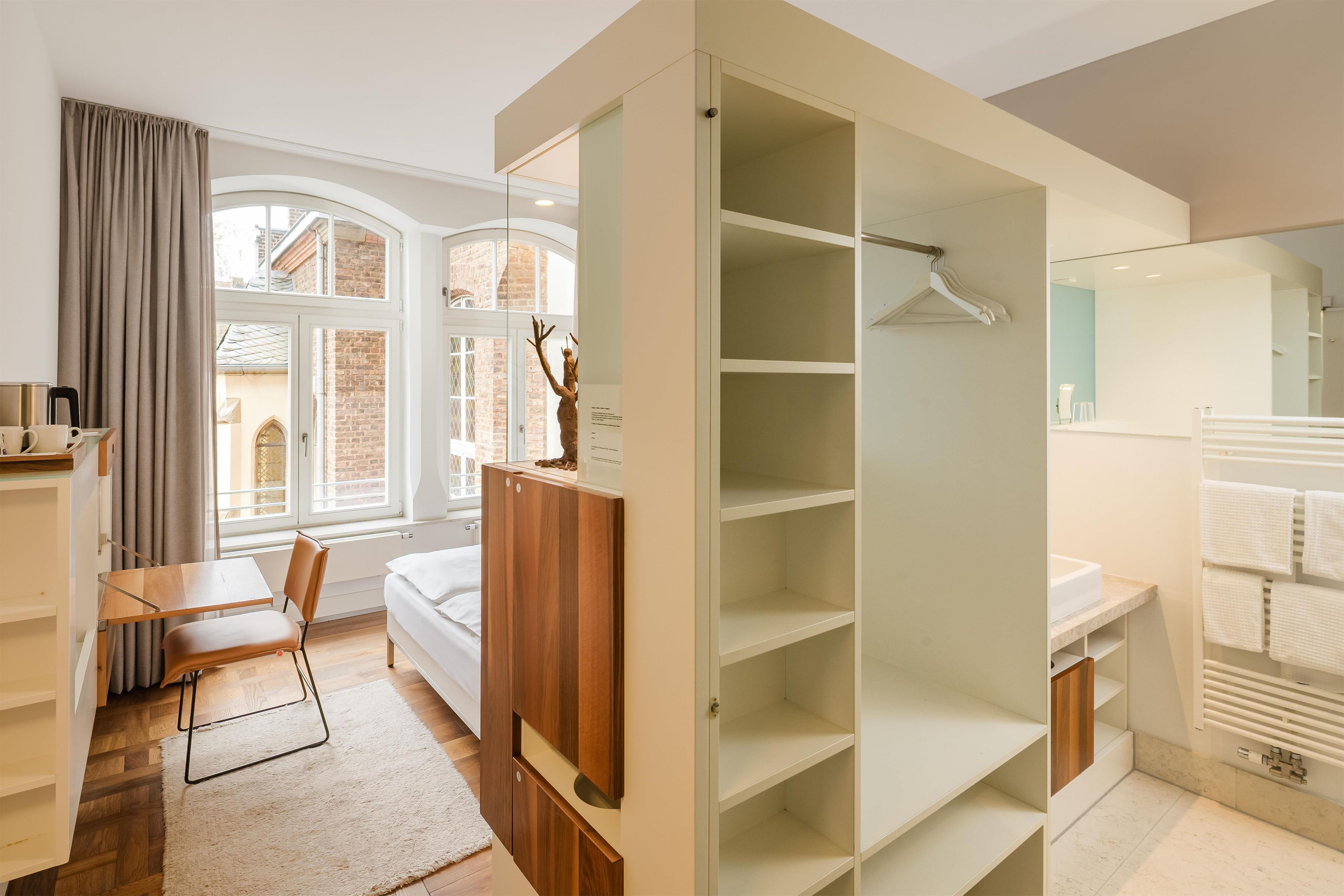 Ein modernes Hotelzimmer mit großem Kleiderschrank, einem Bett, einem Schreibtisch und Blick auf die Stadt.