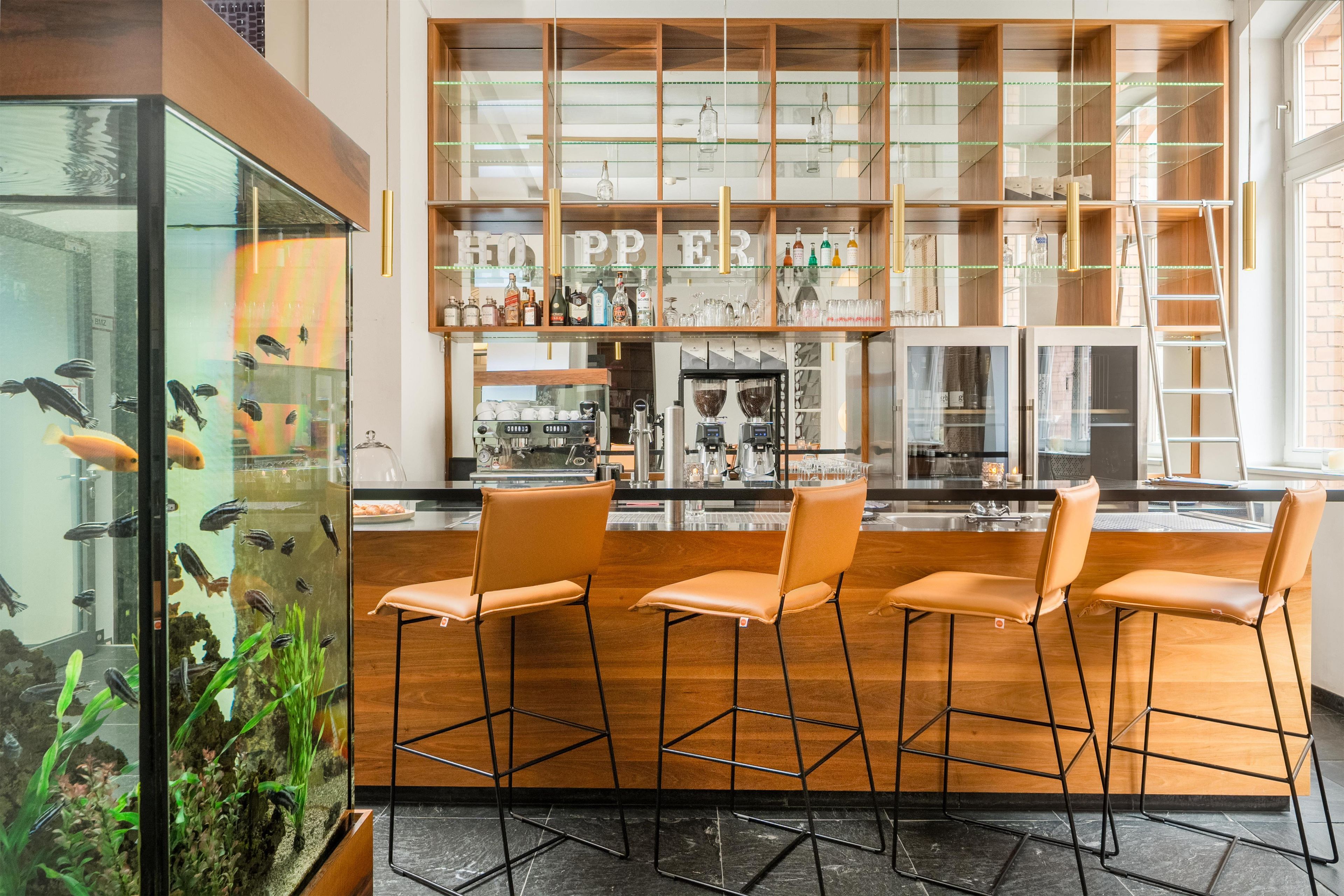 A bar area with wooden bar stools, a fish tank, and shelves with bottles and glasses.