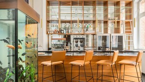 Zona de bar con taburetes de madera, un acuario y estanterías con botellas y vasos.