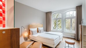 Un dormitorio moderno con una cama grande, mesitas de noche, un escritorio y vistas a árboles por la ventana.