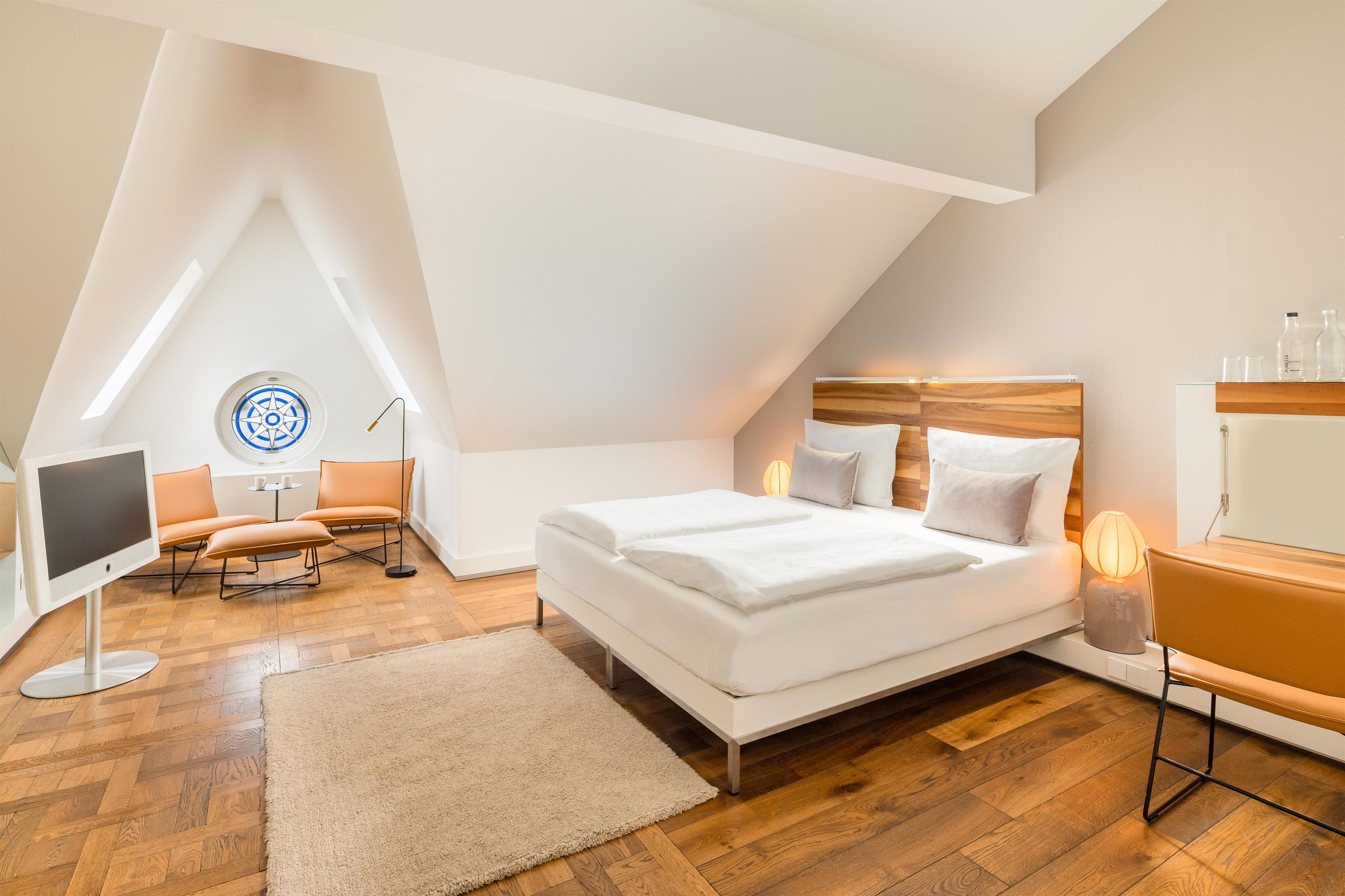 Une chambre moderne avec un plafond en pente, un lit avec une literie blanche, un bureau avec une lampe et une chaise.