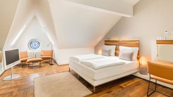 Une chambre moderne avec un plafond en pente, un lit avec une literie blanche, un bureau avec une lampe et une chaise.