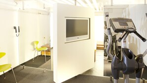 Un gimnasio moderno con equipamiento de ejercicio, una televisión y una zona de estar con una silla.
