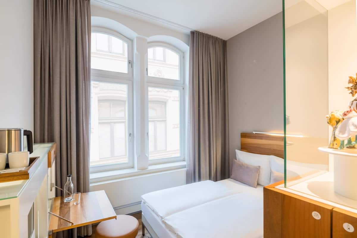 A hotel room with a bed, bedside table, lamp, and a window with curtains.