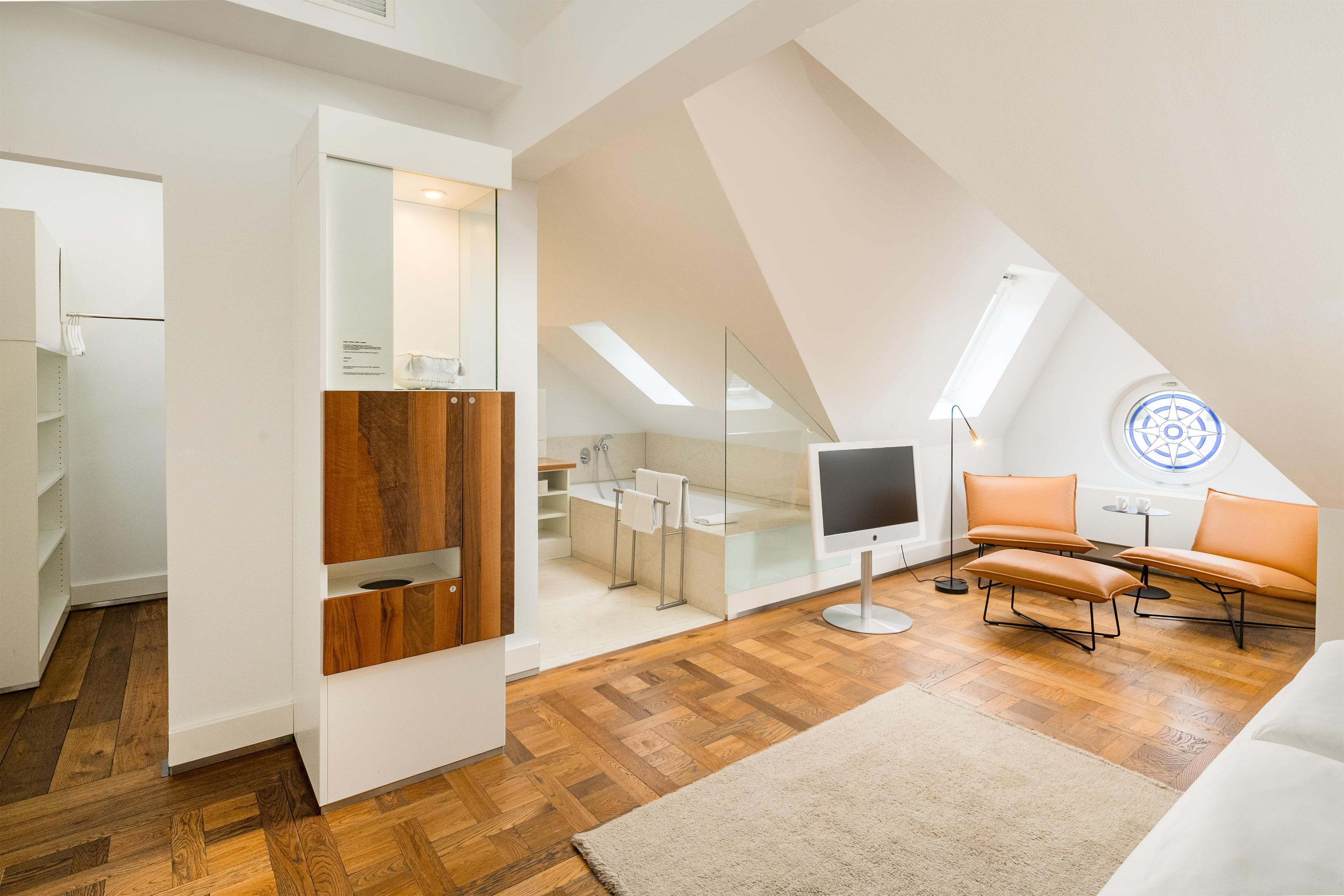 Un dormitorio estilo loft moderno con techo inclinado, piso de madera, un ventanal grande y un rincón de descanso acogedor.