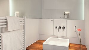 Un baño con un lavamanos blanco, una encimera de madera, un perchero y un florero con una flor.