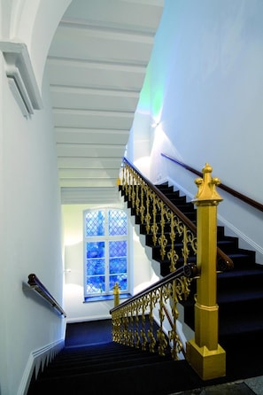 A staircase with black steps and golden balusters, leading to a landing with a blue window. - Hopper Hotel St. Josef, WorldHotels Crafted (Cologne)