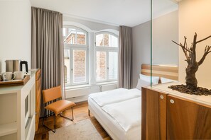 A hotel room with a bed, a desk with a kettle, a chair, and a view of a brick building through the window. - Hopper Hotel St. Josef, WorldHotels Crafted (Cologne)