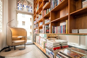 A library with bookshelves, a reading chair, and a stained glass window.