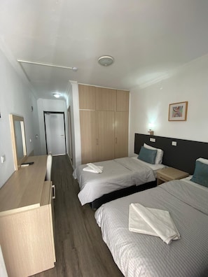 A hotel room with two beds, a wooden wardrobe, a desk, and a mirror.