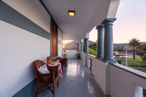 Ein Balkon mit Korbstühlen und einem Tisch, mit Blick auf eine Stadtlandschaft und Berge.