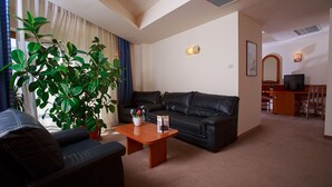 A living room with a sofa, a coffee table, and a potted plant. There is a television and a desk in the background. - Hotel Irisa (Bucharest)