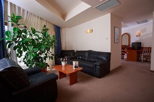 A living room with a sofa, a coffee table, and a potted plant. There is a television and a desk in the background.