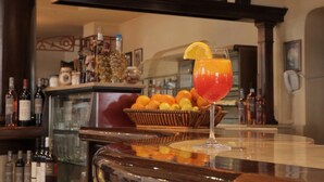 A bar area with a glass of red cocktail garnished with an orange slice, a basket of oranges, and various bottles of alcohol on shelves. - Hotel Irisa (Bucharest)