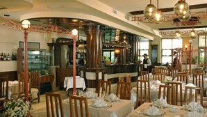 A restaurant with tables set for dining, a bar area, and a kitchen in the background. - Hotel Irisa (Bucharest)
