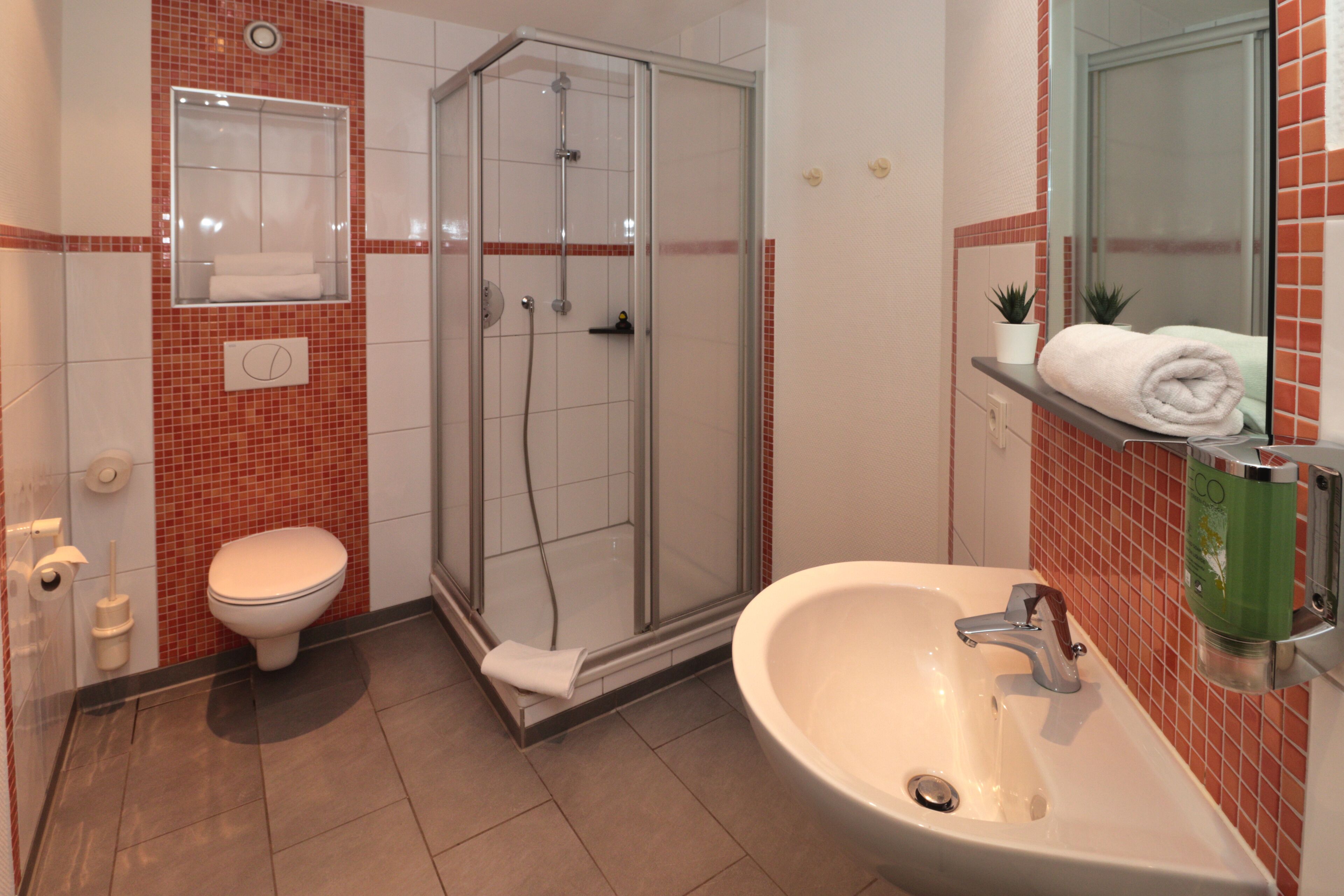 A bathroom with a glass-enclosed shower, a toilet, and a sink with a mirror above it.