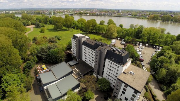A modern building complex with multiple high-rise structures, a parking area, and a river in the background. - DJH City-Hostel Köln-Riehl (Cologne)