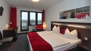 A hotel room with a large bed, a desk, a chair, and a window with a view. - DJH City-Hostel Köln-Riehl (Cologne)