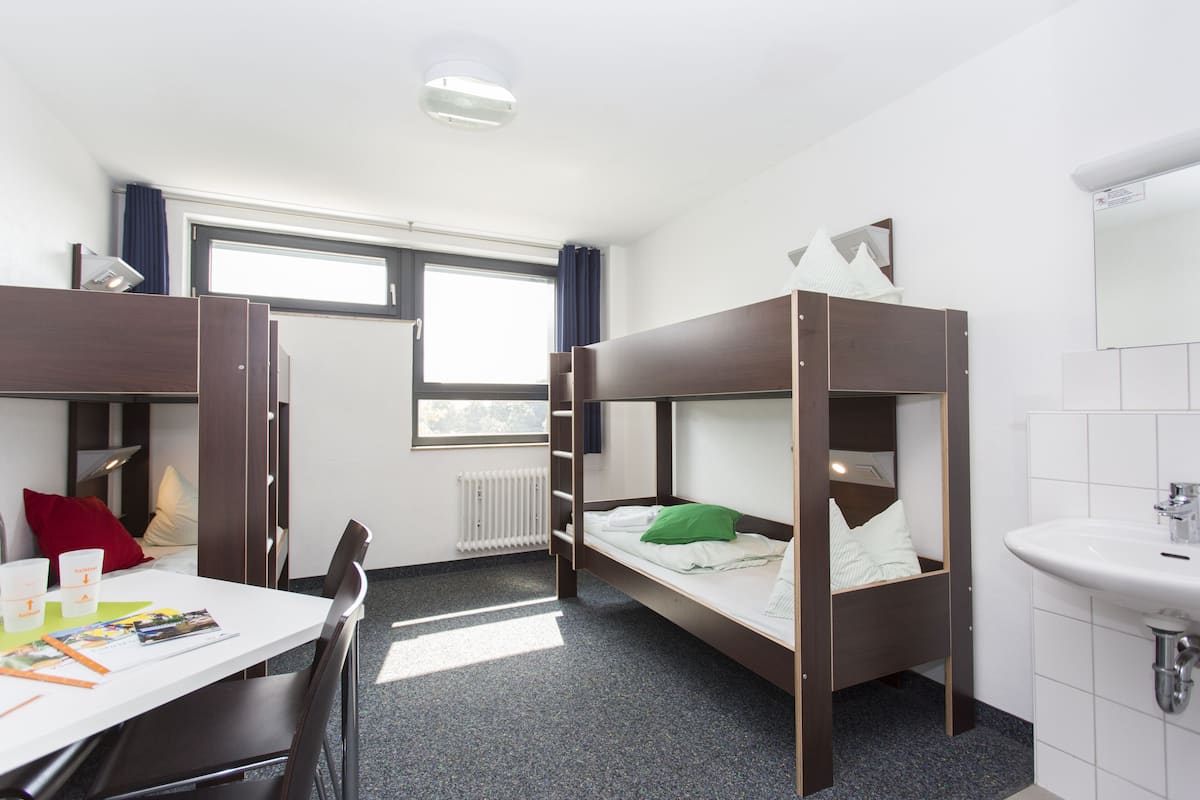 Un dormitorio con literas, un escritorio, una silla, una ventana y un baño con lavamanos.