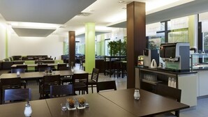 A modern dining area with multiple tables and chairs, a coffee machine, and a large window providing natural light. - DJH City-Hostel Köln-Riehl (Cologne)