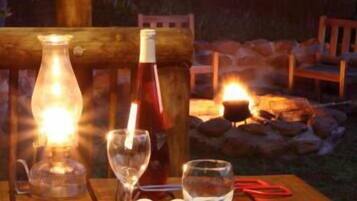 A wooden dining table set outdoors with a candle, wine bottle, and glasses.