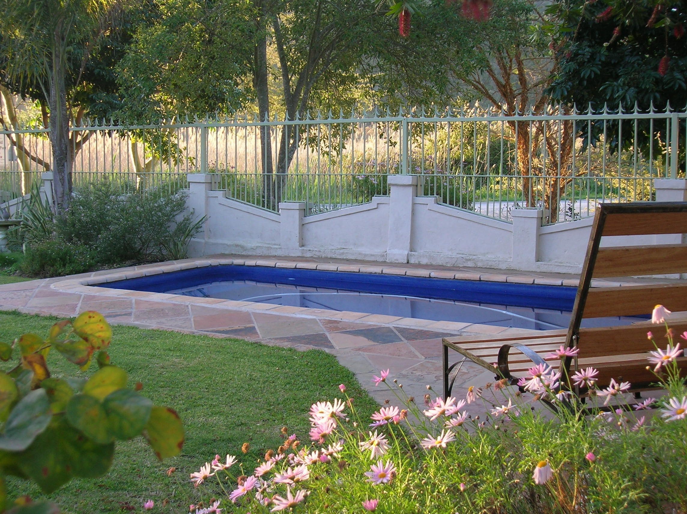 A swimming pool with a stone deck, surrounded by a white fence and lush greenery.