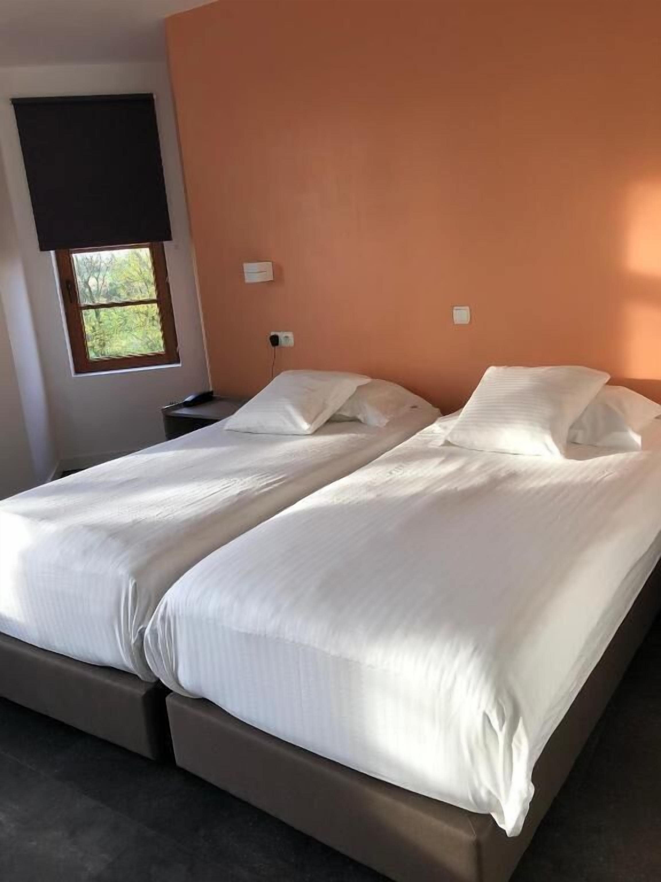 Una cama doble con sábanas blancas en una habitación con pared naranja.