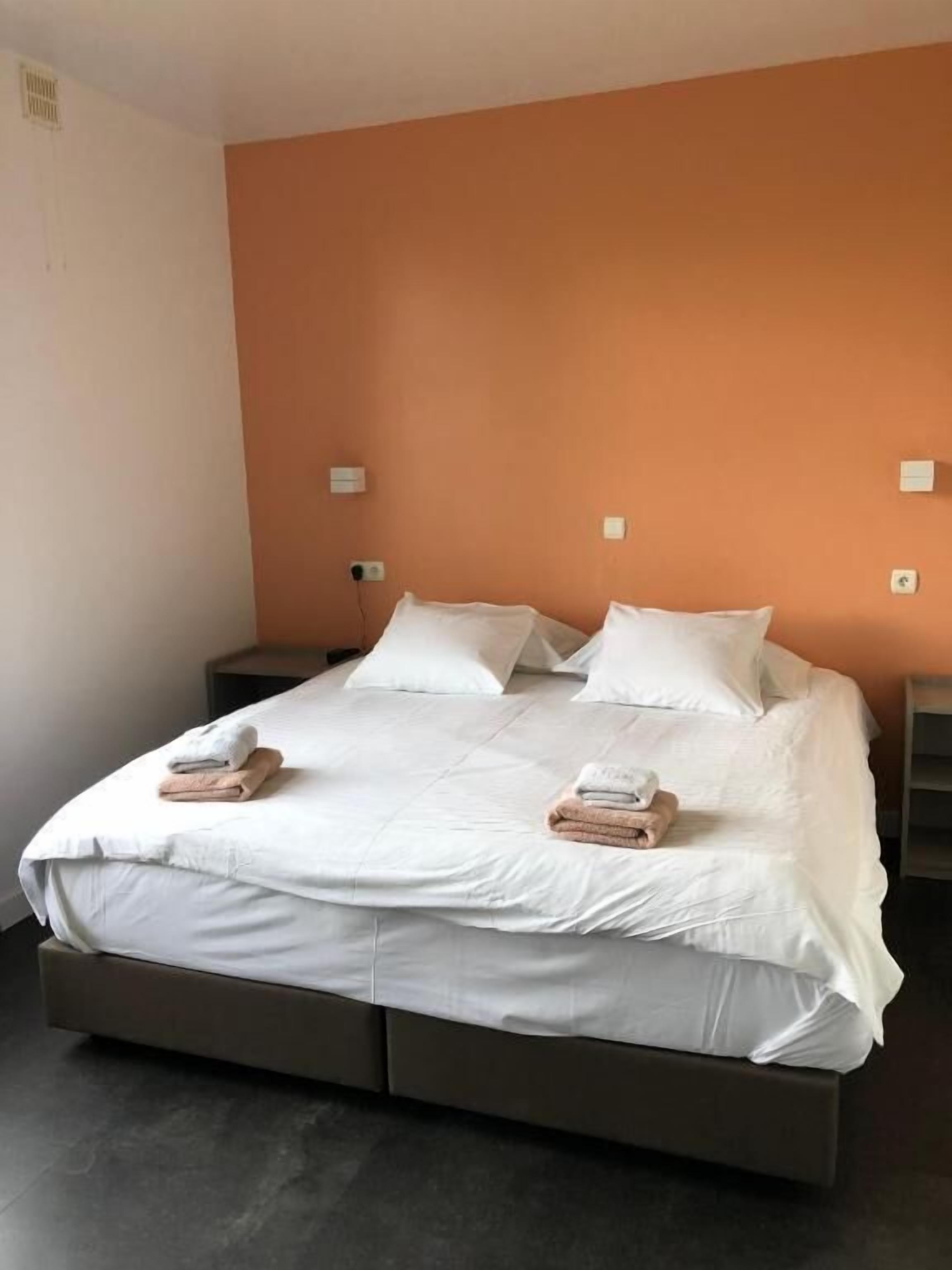 A bed with white bedding, two pillows, and two folded towels.
