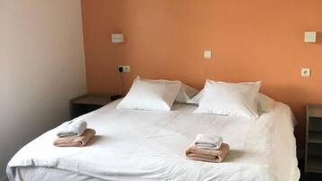 A bed with white bedding, two pillows, and two folded towels.