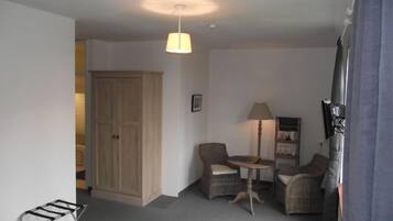 A small, cozy room with a wooden wardrobe, two wicker chairs, a small table, and a hanging light fixture.