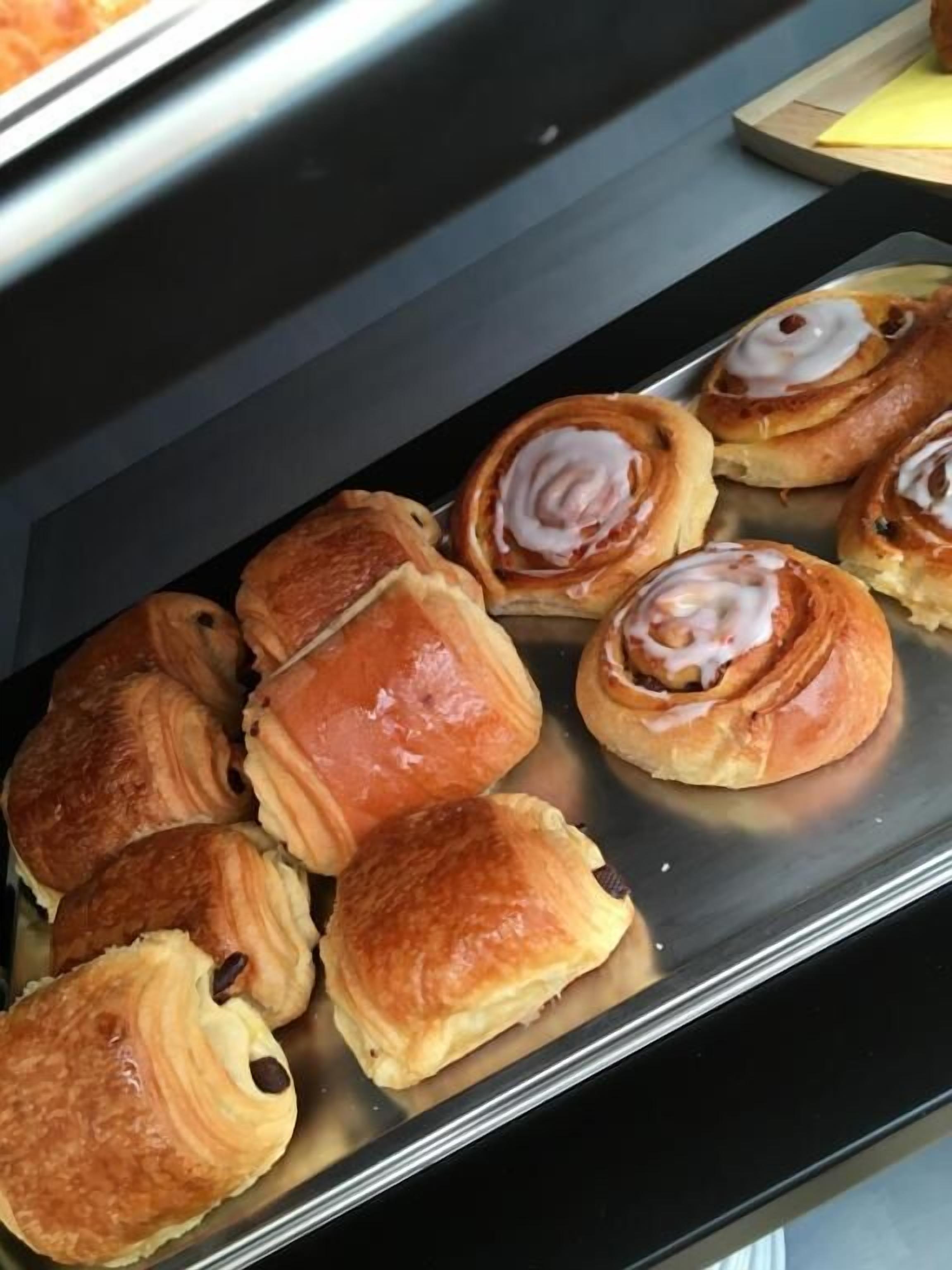 Una bandeja de pasteles, incluyendo rollos de canela y croissants, sobre una superficie metálica.
