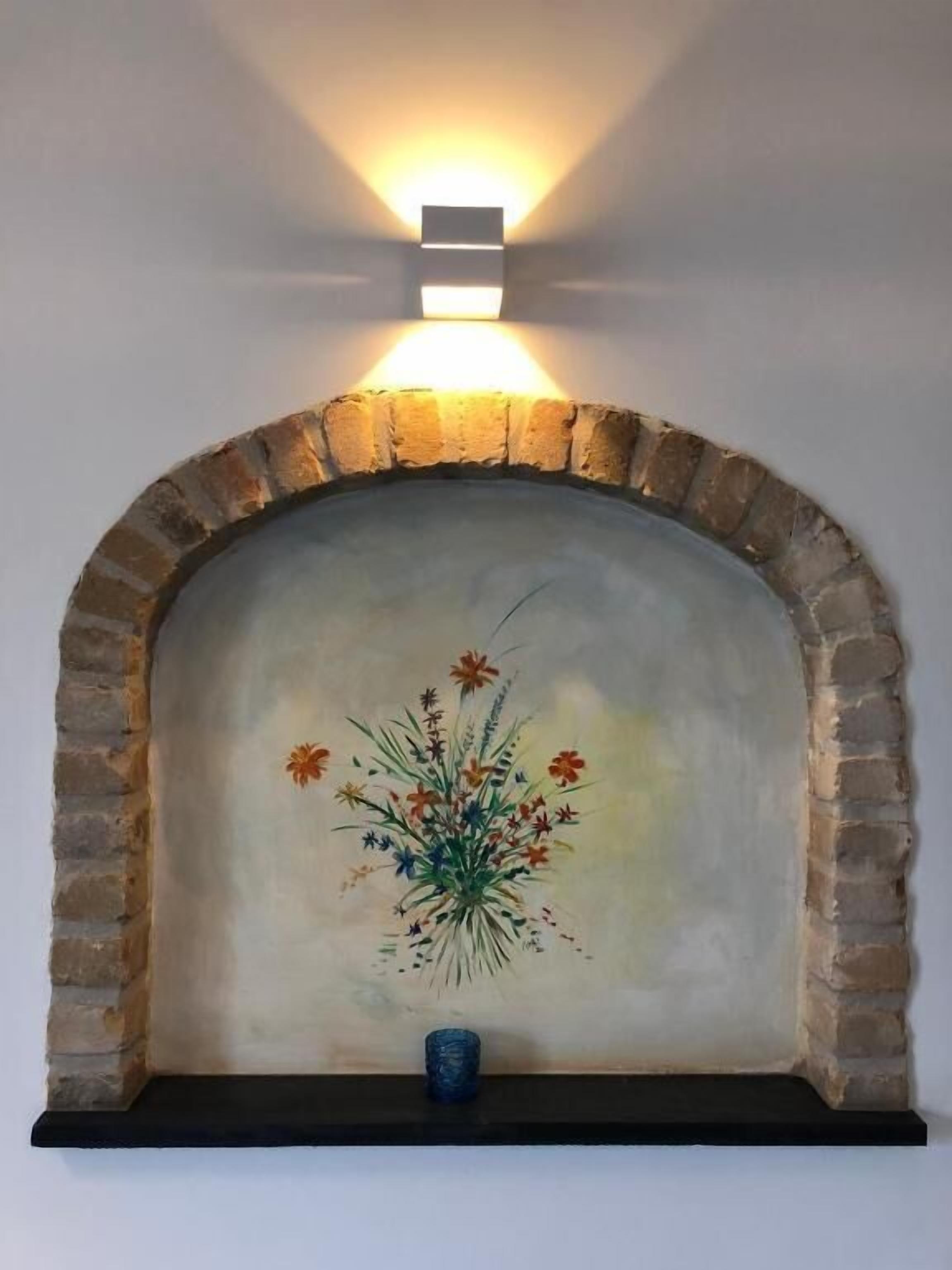 A fireplace with a painted floral design and a blue vase below it.