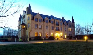 A large, historic building with multiple windows and a prominent entrance, surrounded by a well-maintained lawn.