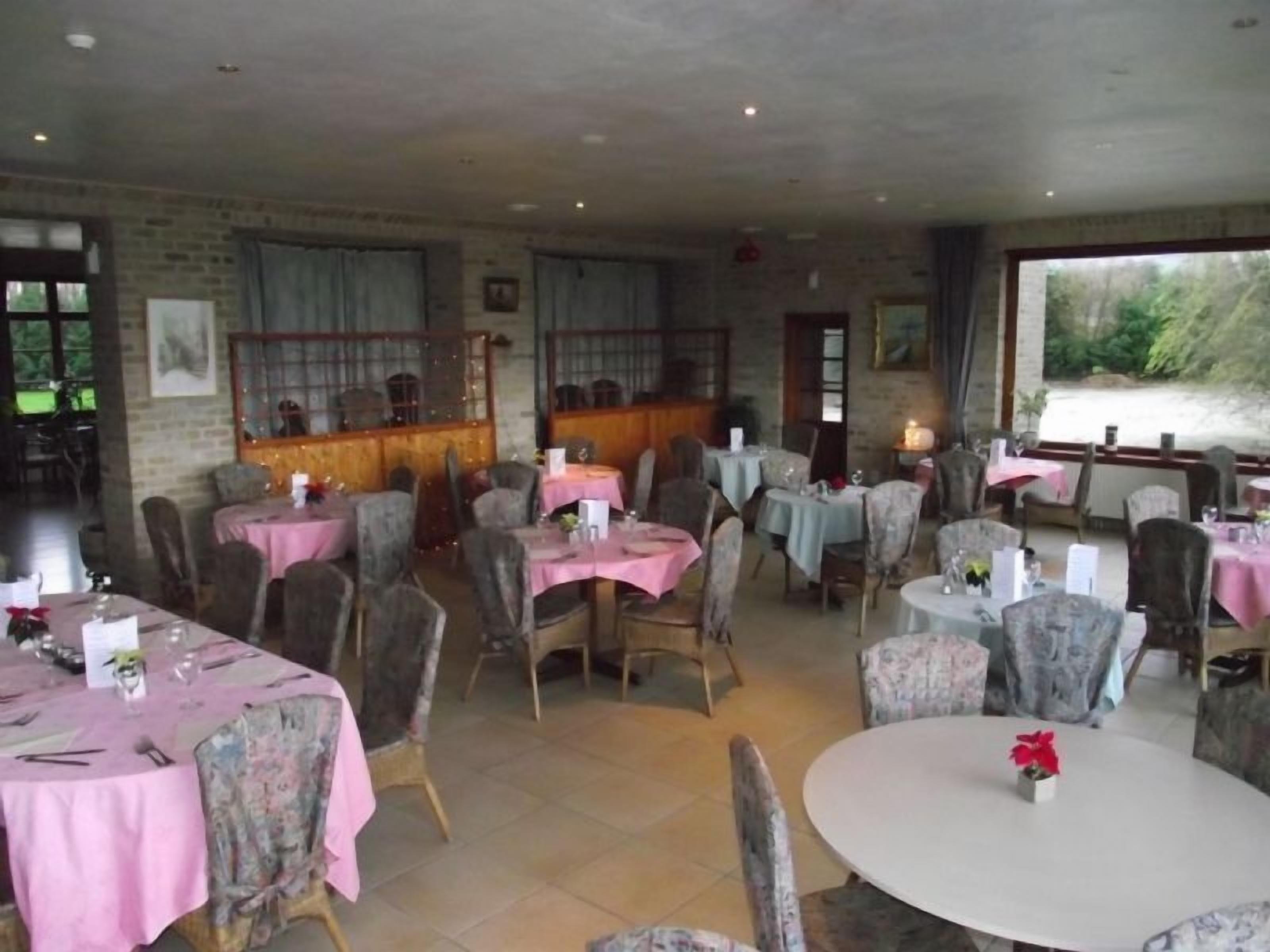 A restaurant with round tables covered in pink tablecloths, surrounded by upholstered chairs.