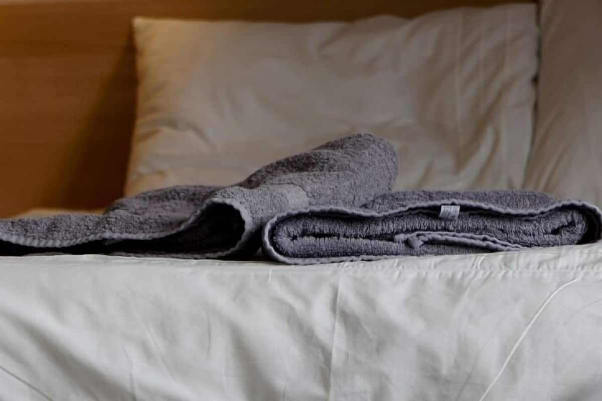 A bed with a folded gray towel and a white pillow.
