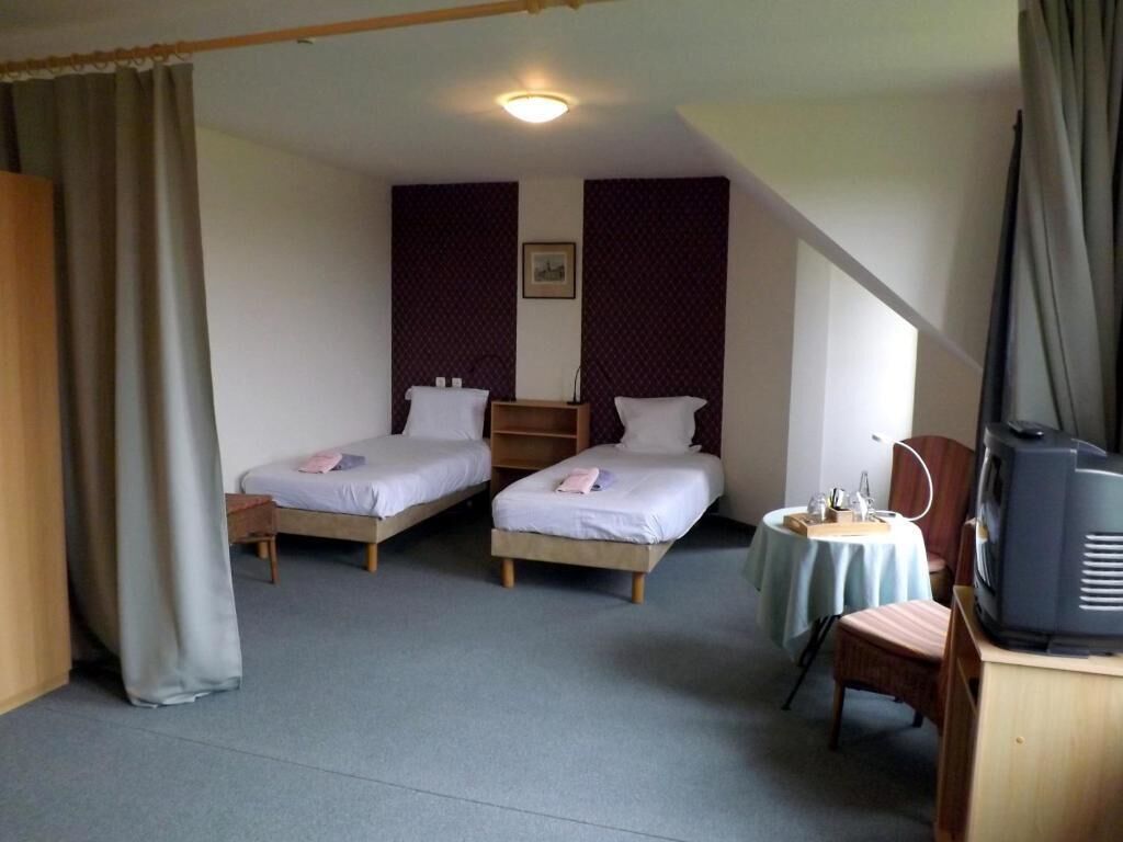 A room with two single beds, a small table with a chair, a television, and a ceiling light.