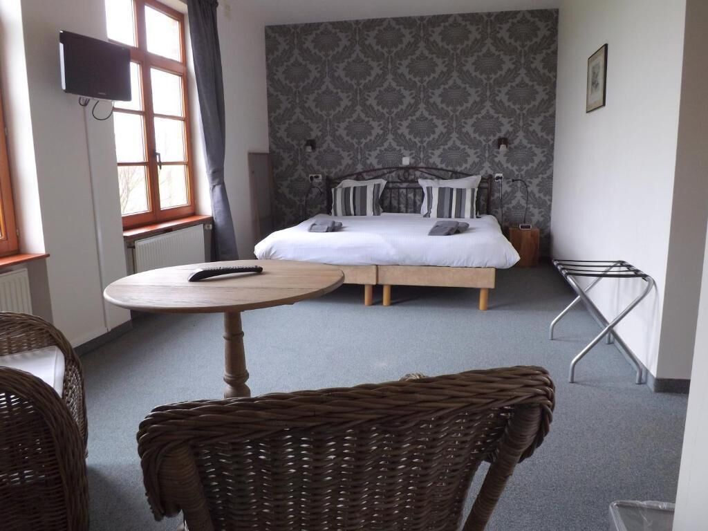 Un dormitorio con una cama, una mesa redonda y una silla de mimbre.