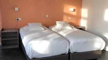 Una cama doble con ropa blanca en una habitación con una pared de acento naranja y suelo oscuro.