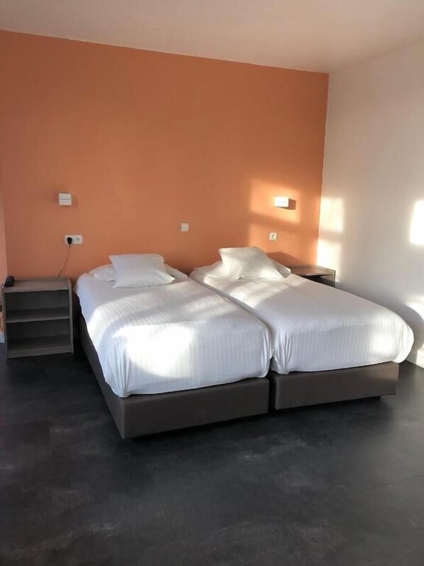 A double bed with white linens in a room with an orange accent wall and a dark floor.