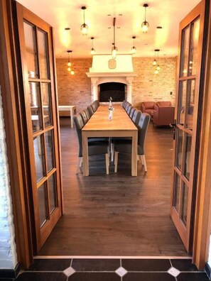 A dining area with a long wooden table, cushioned chairs, and pendant lighting.