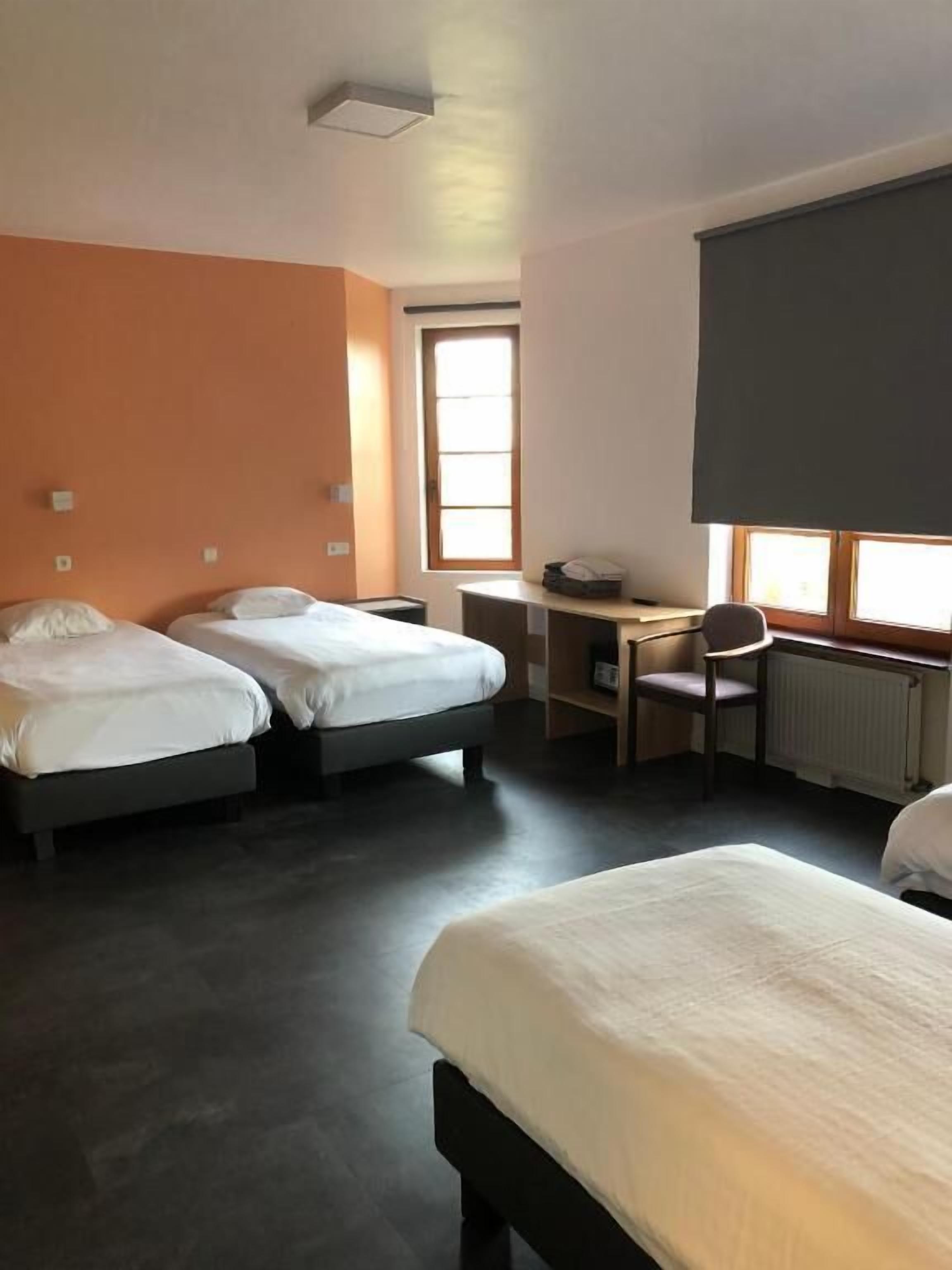 Une chambre d’hôtel avec deux lits simples, un bureau, une chaise et une grande fenêtre.