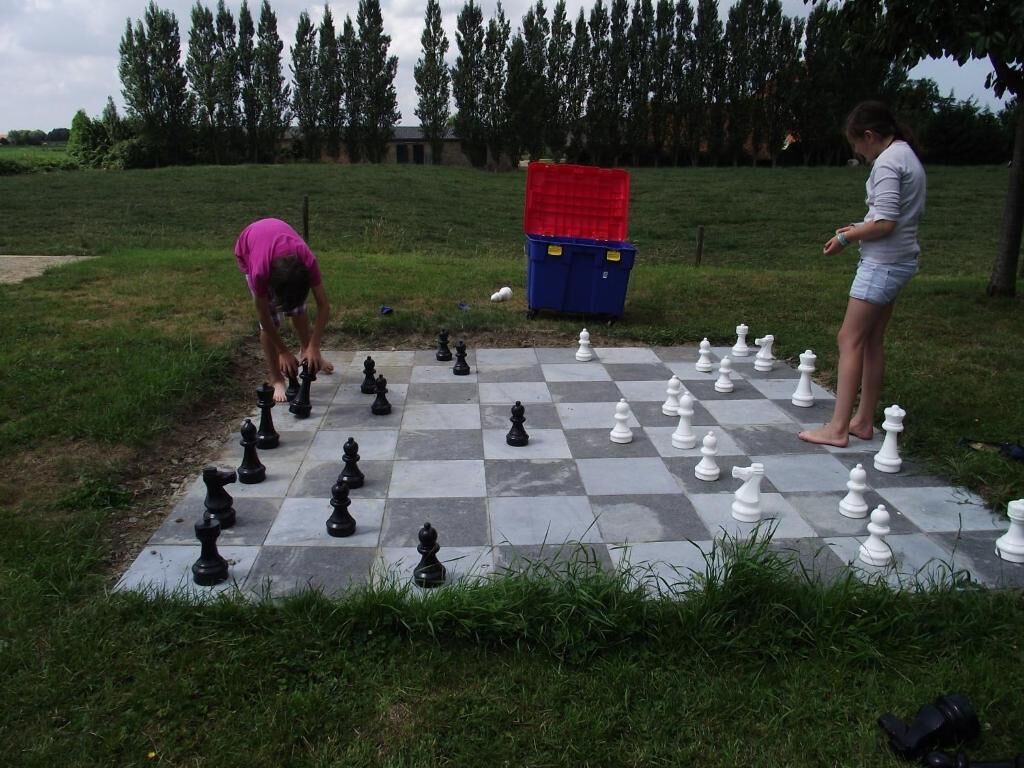 A chessboard set up outdoors with a red container and a blue container in the background.