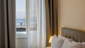 A hotel room with a bed, a window with curtains, and a view of the sea. - Hotel Vis a Vis (Trieste)