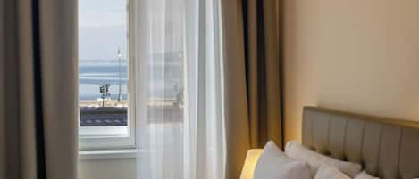 Habitación de hotel con cama, ventana con cortinas y vista al mar.